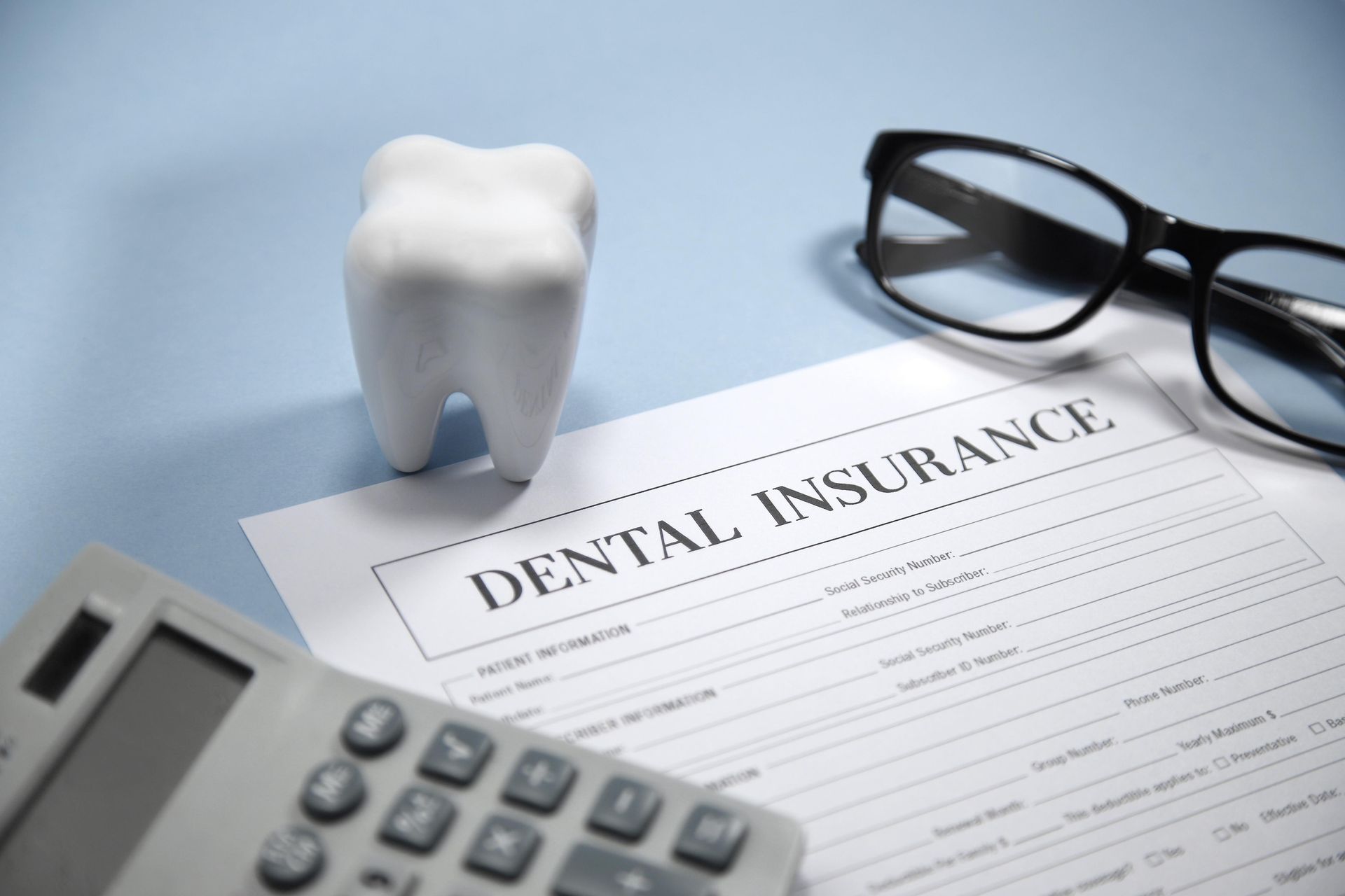 A tooth is sitting on top of a dental insurance form next to a calculator and glasses.