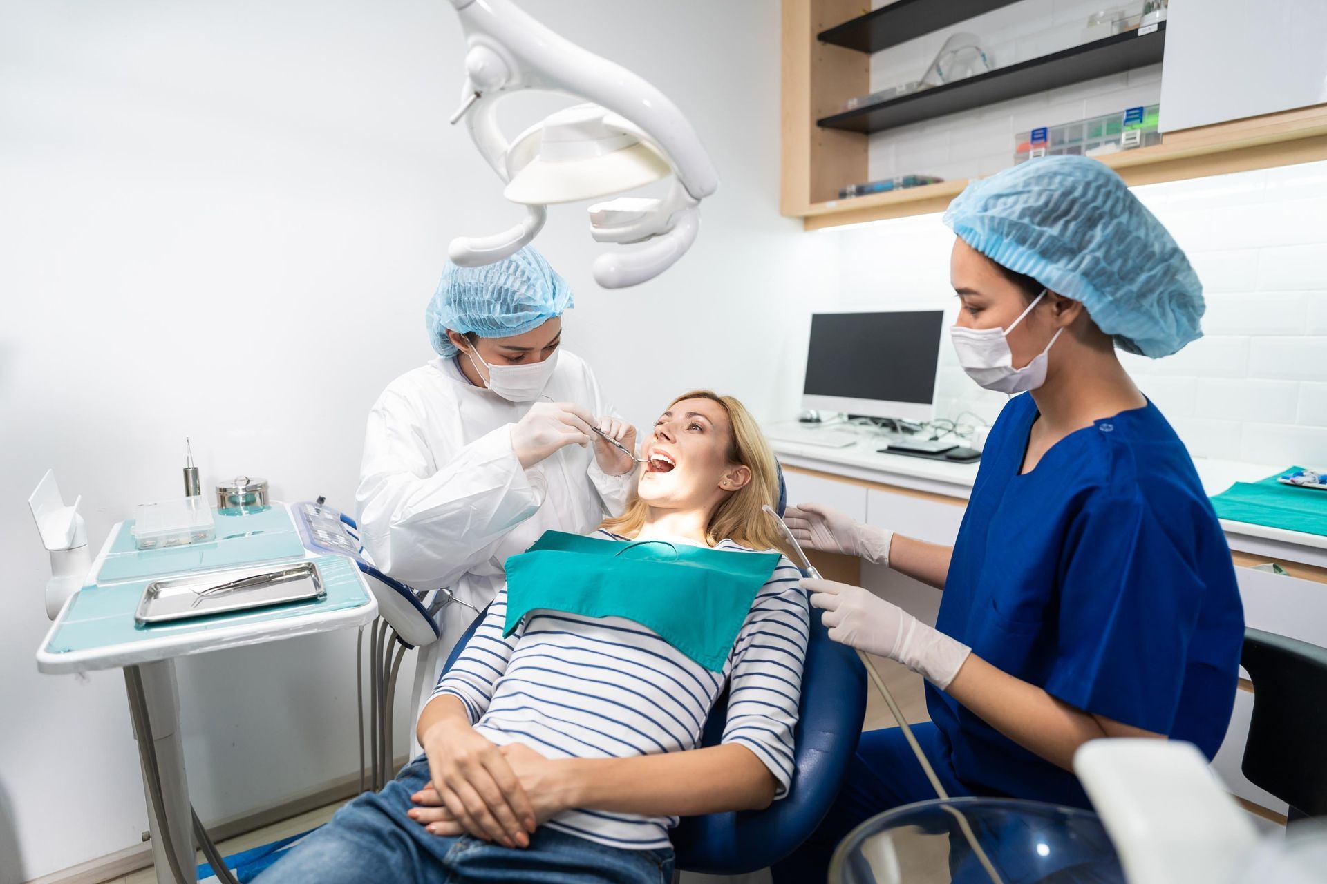 A woman is sitting in a dental chair getting her teeth examined by two dentists.