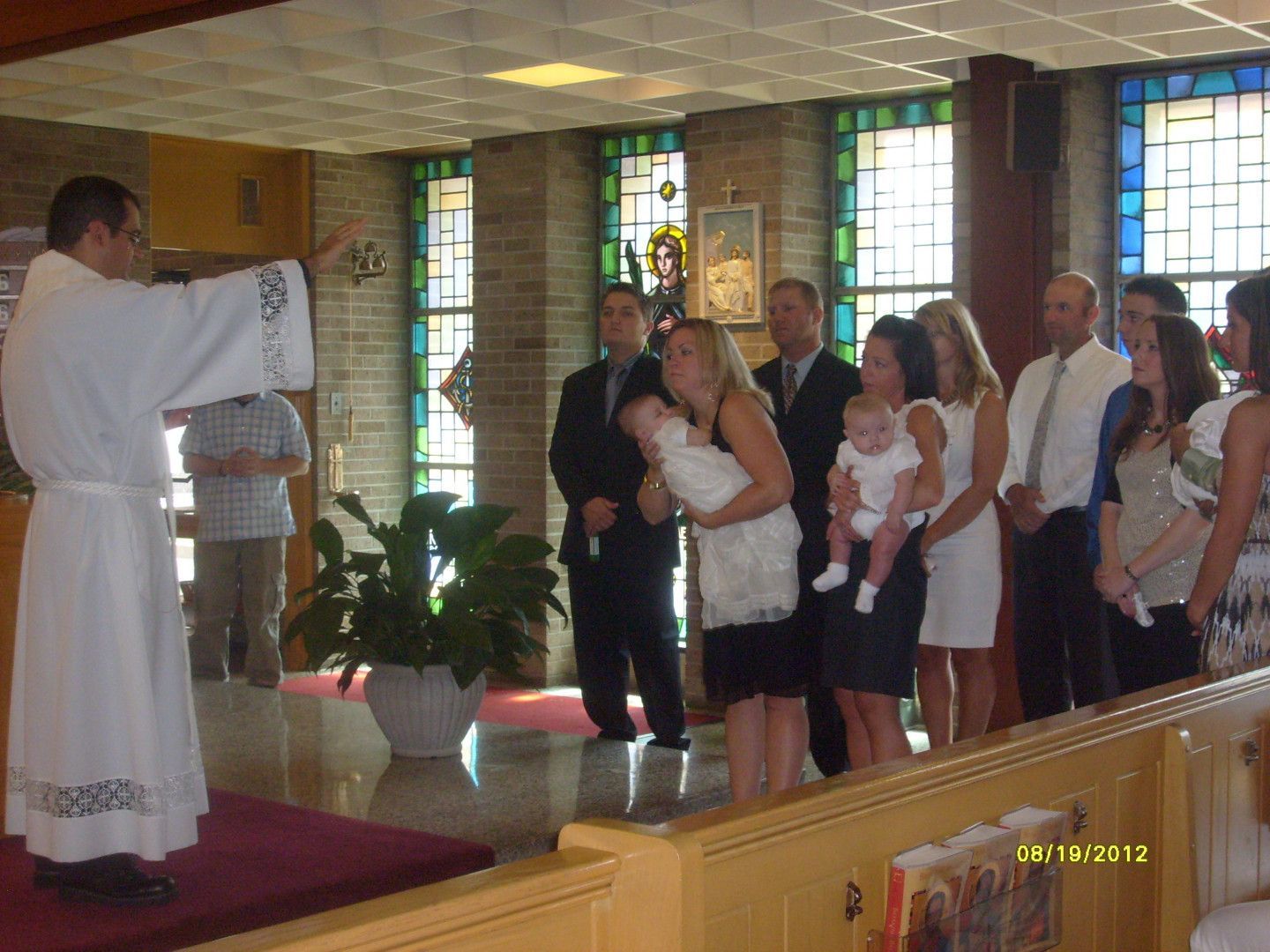 Priest blessing babies during a christening ceremony in a church. People in formal attire watch.