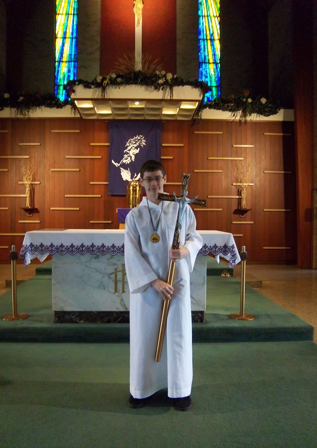 Person in white robe holding a staff in front of an altar in a church.