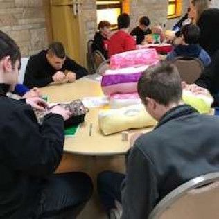 People seated at a table, working on a craft project. Several plush items are on the table.