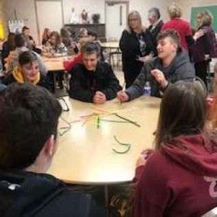 People at a table, playing a game with green pipe cleaners.