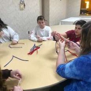 People seated around a table, working with small, colorful craft materials.