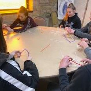 People around a table working with strings.