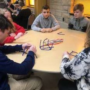 People seated around a table, working with pipe cleaners.