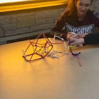 Woman making a geometric shape with colorful pipe cleaners on a table.