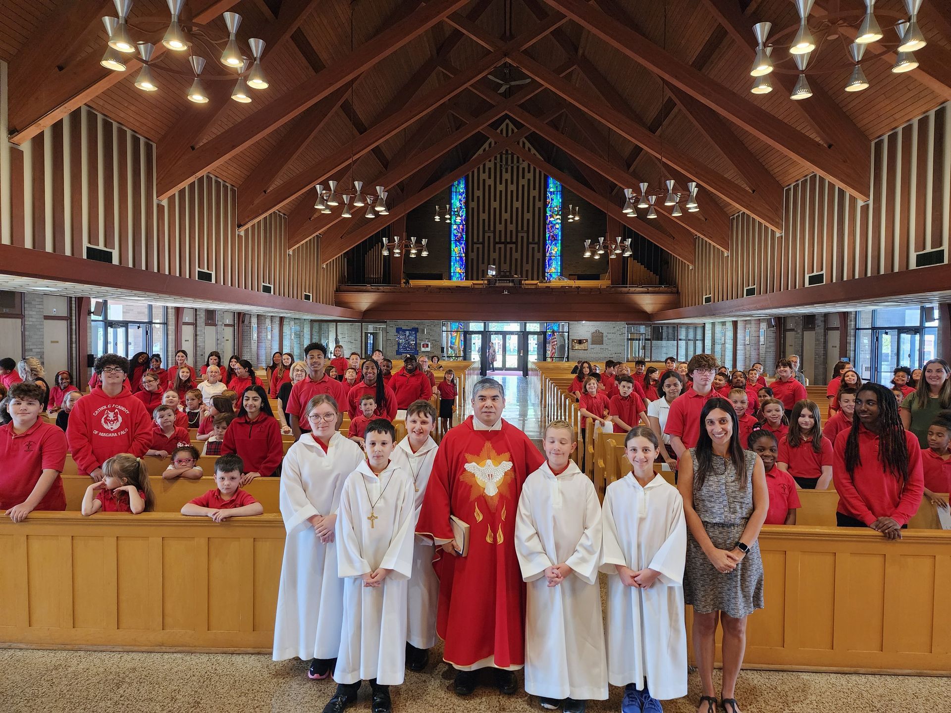 Group of people in red shirts and white robes, with a priest in a church setting.