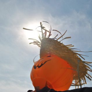 Orange pumpkin decoration with straw hat, smiling face against sunny sky.