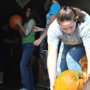 People picking pumpkins. One woman bends to lift a pumpkin, others hold pumpkins inside a dark doorway.