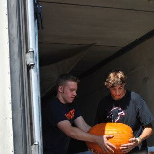 Two people loading a large pumpkin into a truck.