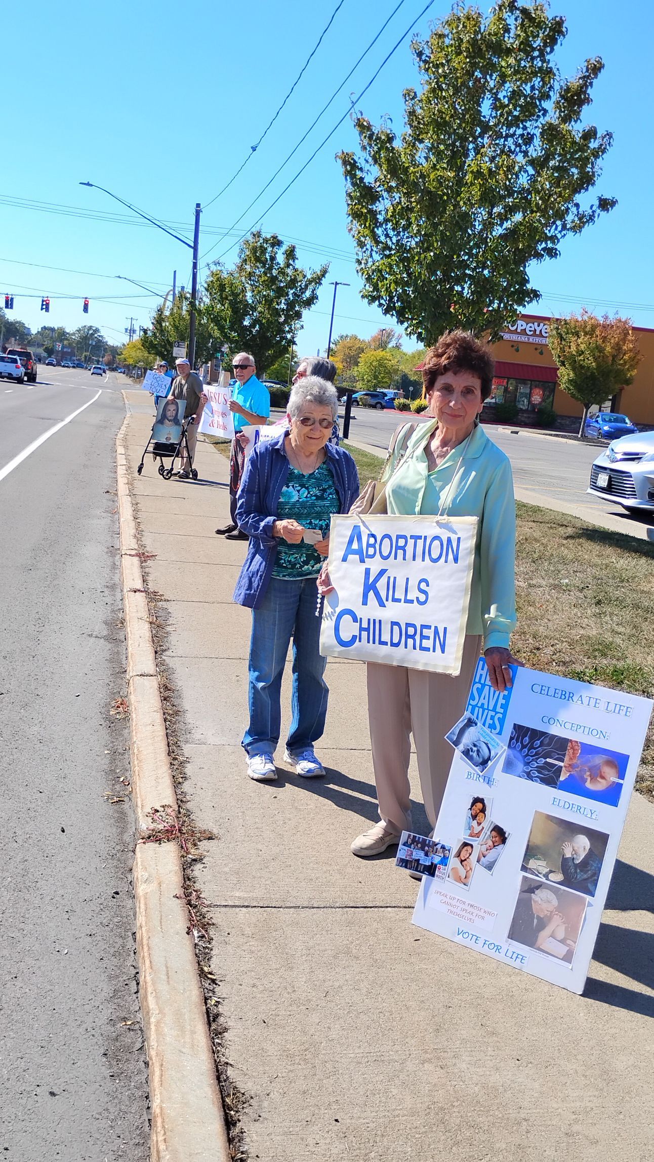 People protesting on a sidewalk, holding signs that say 