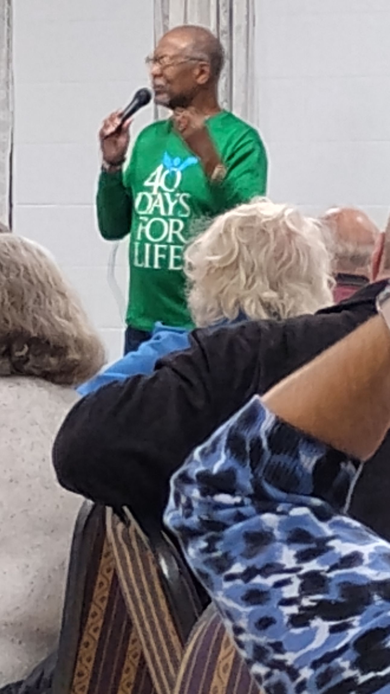 Man speaking into a microphone, wearing a green 