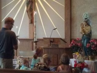 People in a church, focused on a statue of Mary with Jesus.  A man and several children are praying near a crucifix.