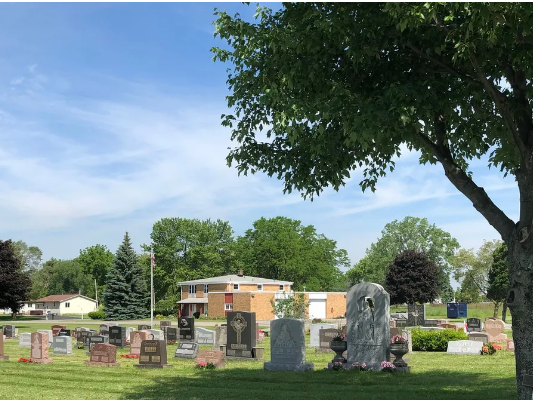 Cemetery on a sunny day with headstones, a building, and trees. Blue sky overhead.