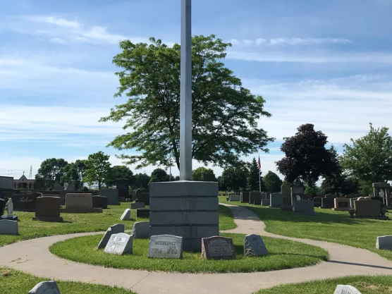 Flagpole in a cemetery, surrounded by headstones and green grass under a blue sky.