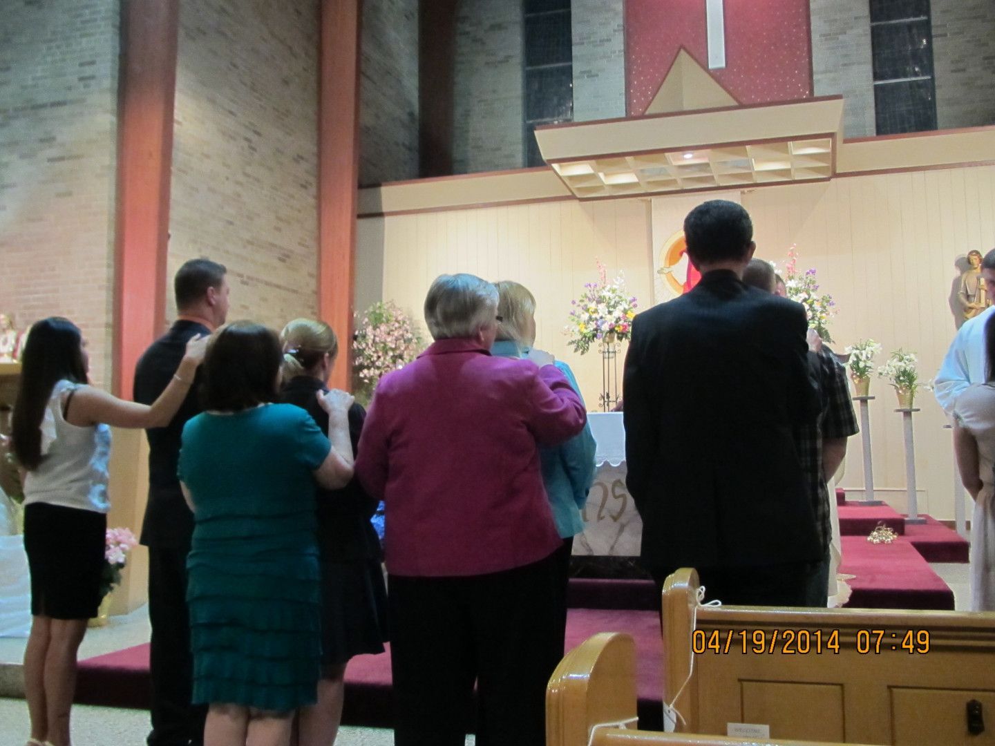 People gathered near an altar, some with hands on others' shoulders; likely a church service.