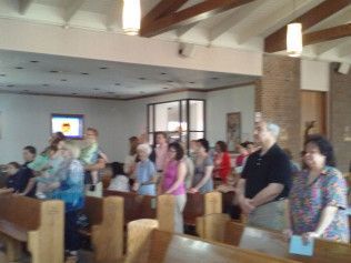 People standing in a church interior, some singing, some with hands clasped in prayer.