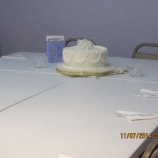 White cake with decorations on a white table. A blue gift bag is nearby.
