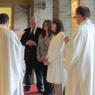 People at a baptism in a church, officiated by two priests.