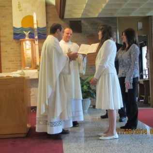Ceremony in church: Priest, two people in white holding book, other person.