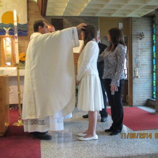 A priest laying hands on a person in white dress during a religious ceremony inside a church.