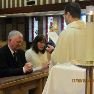 Couple at altar with priest during a religious ceremony; indoor setting.