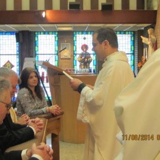 Priest reading at altar during a church service; woman, and other people observe.