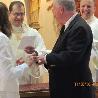 Couple exchanging rings during a wedding ceremony in a church, officiated by two priests.
