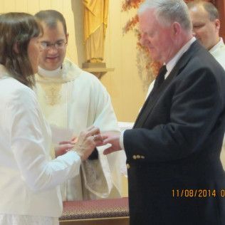 Man and woman exchange rings during a wedding ceremony at a church, officiated by a priest.