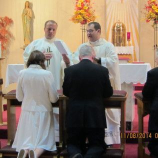 People kneeling at an altar as two priests officiate a ceremony in a church.