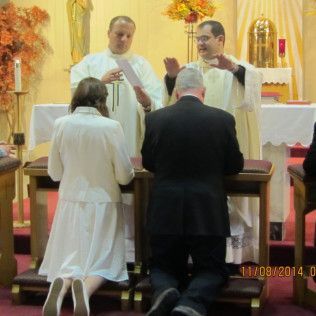 People kneeling at an altar as priests officiate a religious ceremony.