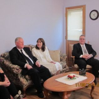Three people in formal wear sit in a living room, near a coffee table.