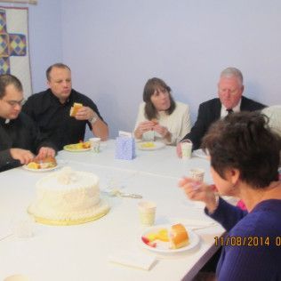 People at a table eating, including cake. Some in formal attire. Light blue walls, date stamp.