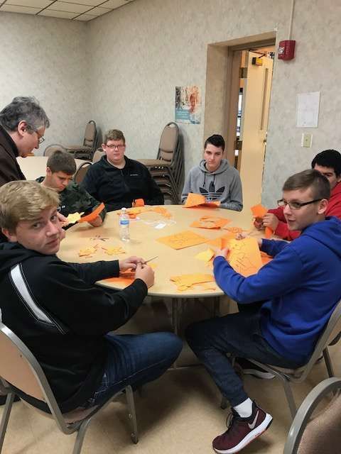 Group of people around a table cutting orange paper, possibly for a craft project.