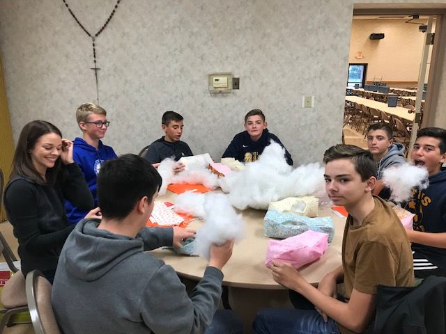 Group of teens around a table stuffing fabric with cotton. Room setting.