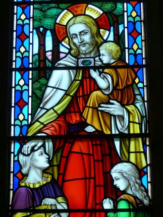 Stained glass: Jesus with child, surrounded by children, in red, white, yellow, and blue hues.
