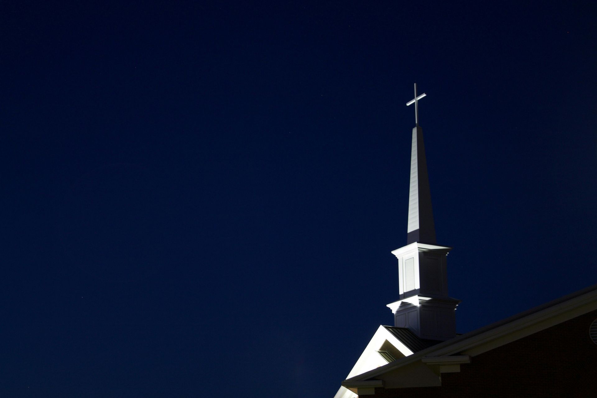 White steeple with cross against a dark blue sky.