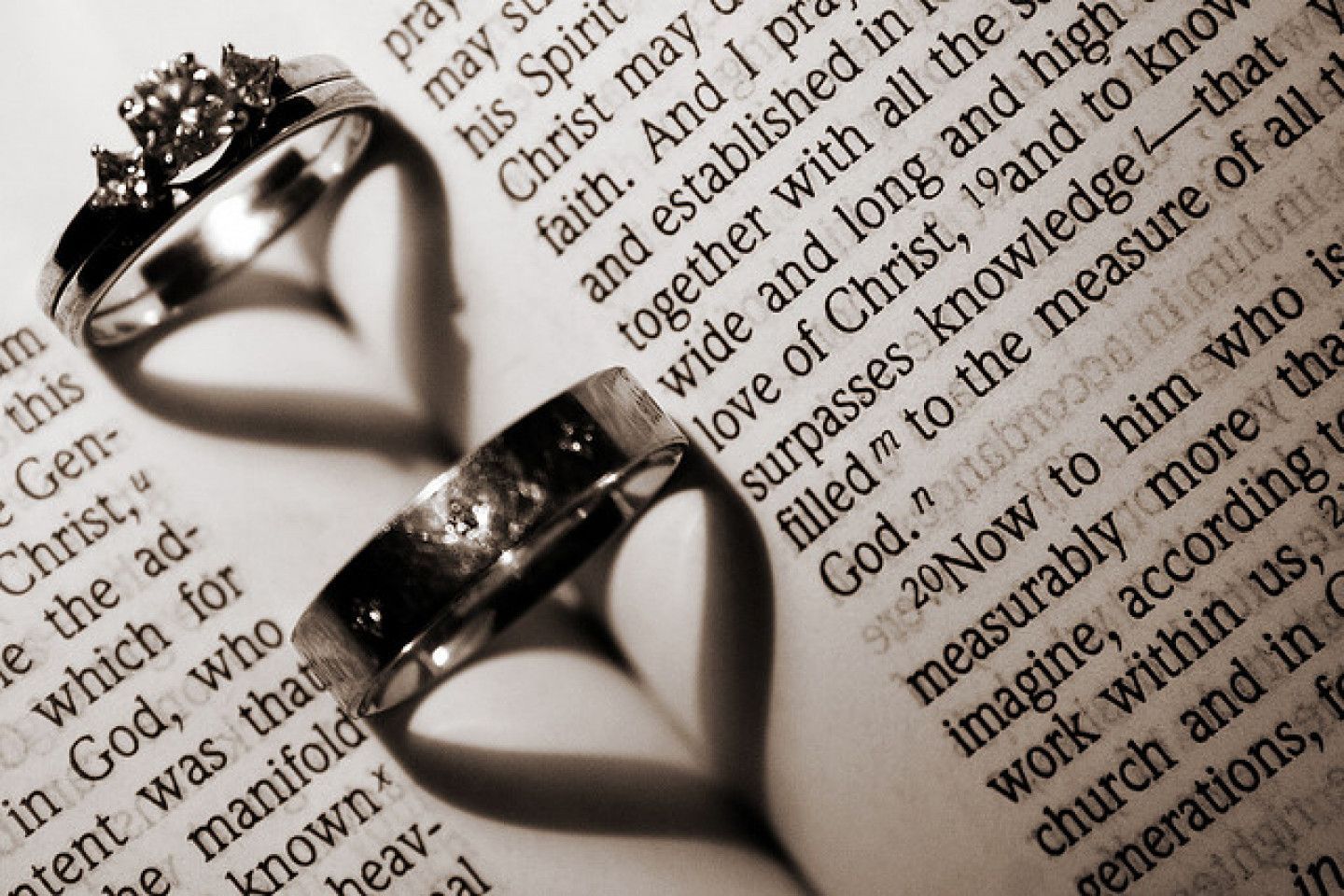 Two wedding rings on an open book, casting a heart-shaped shadow.