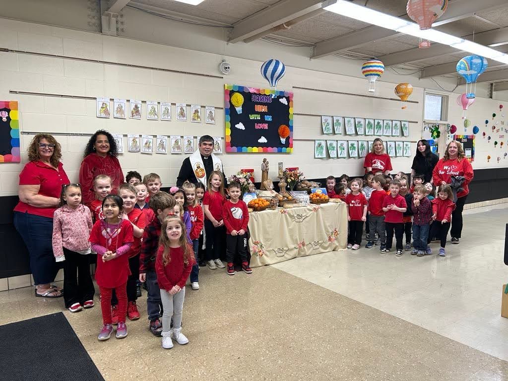 Children and adults in red shirts stand in front of a table with decorations, likely for a school event.