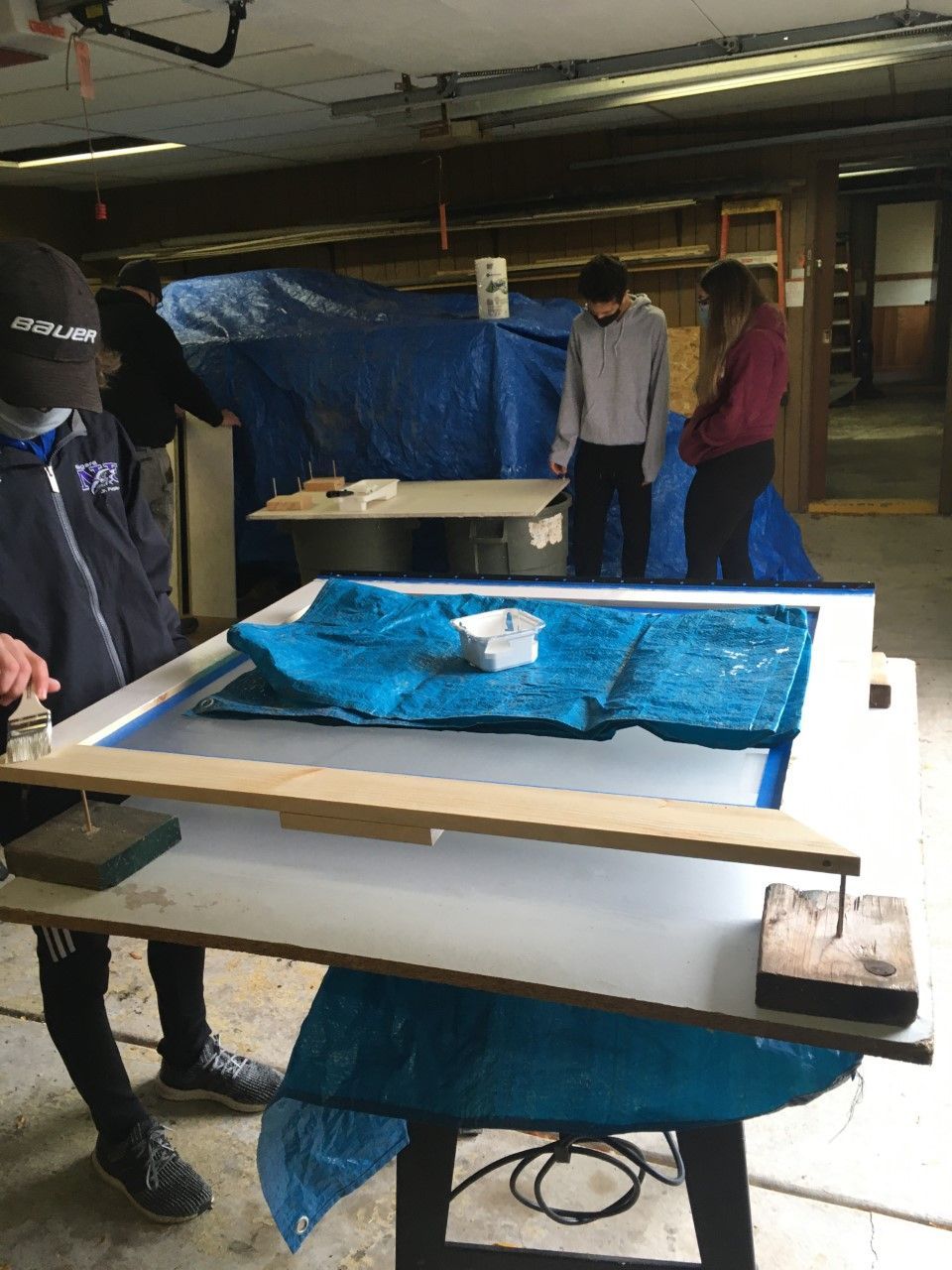 Students working on a craft project inside a garage, pressing a blue material between frames.