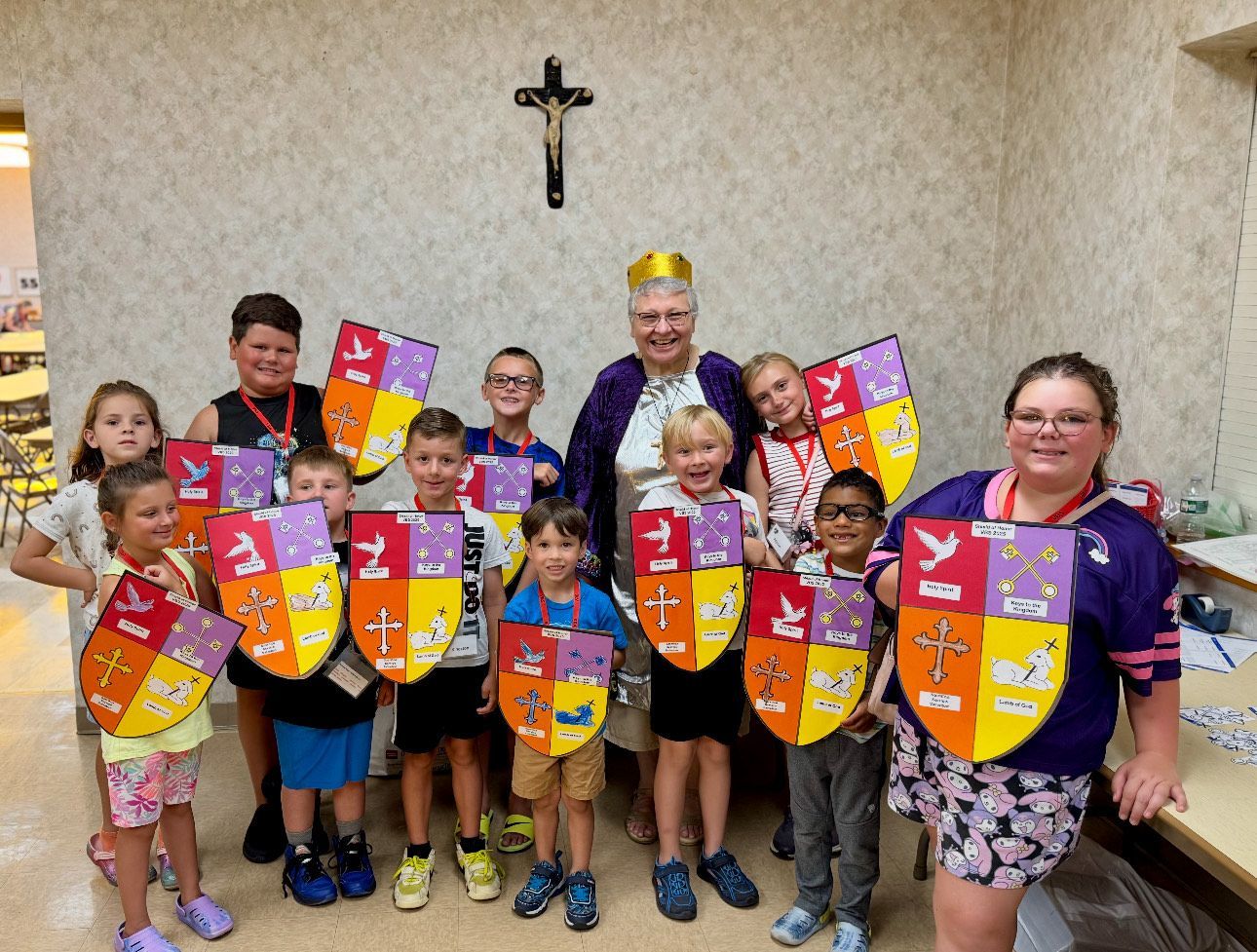 Children and an adult with shields, indoors. The adult wears a purple robe and crown.