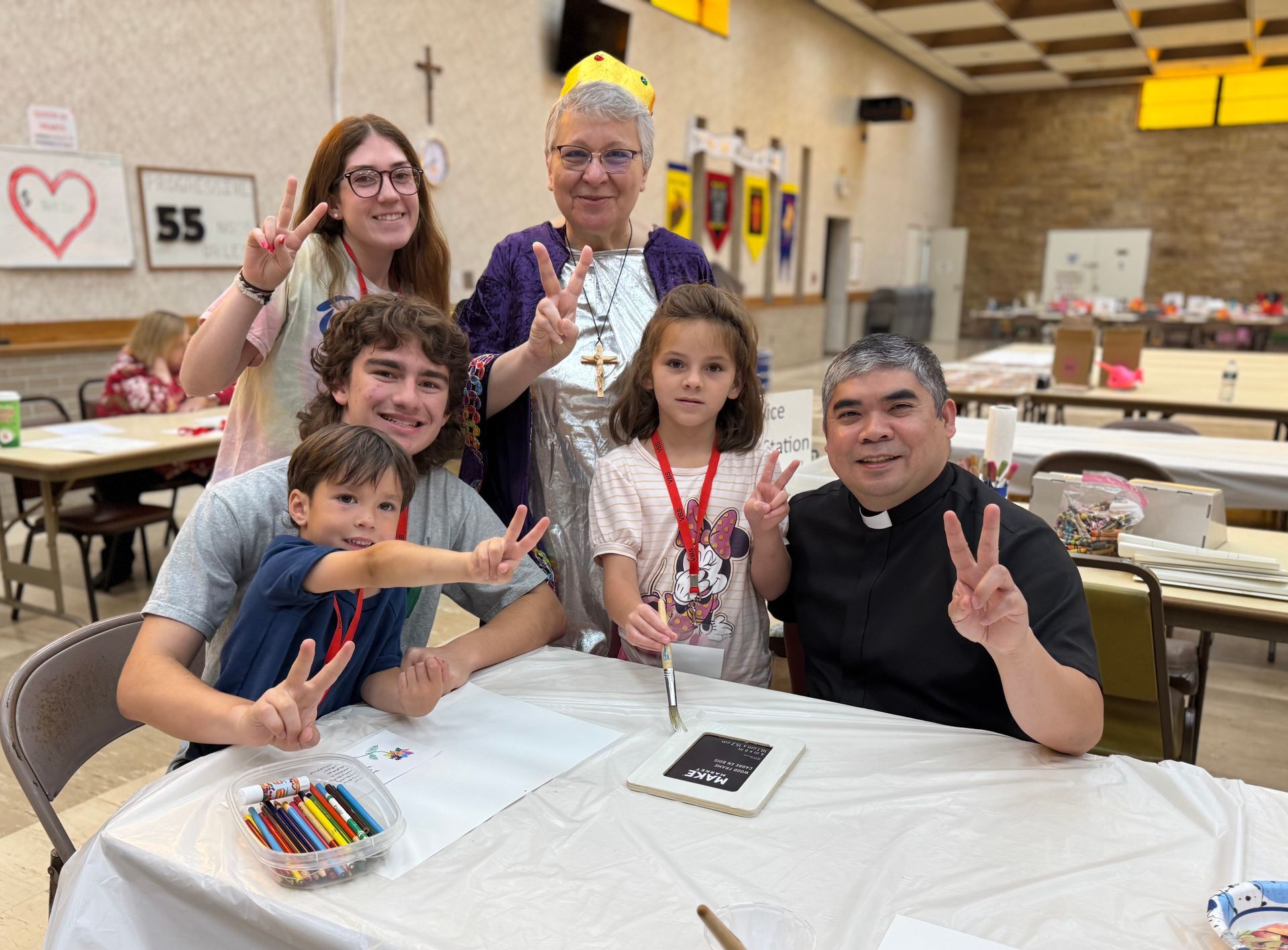 Group of people at a table, making art. All are smiling and giving the peace sign.