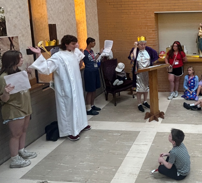 Children in a church act out a scene; one dressed as a king with a crown, others in costumes.