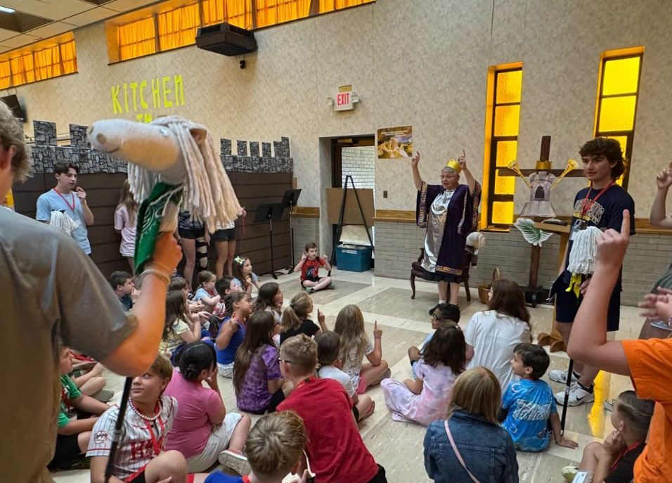 Children sit and watch a costumed person in a room with a 