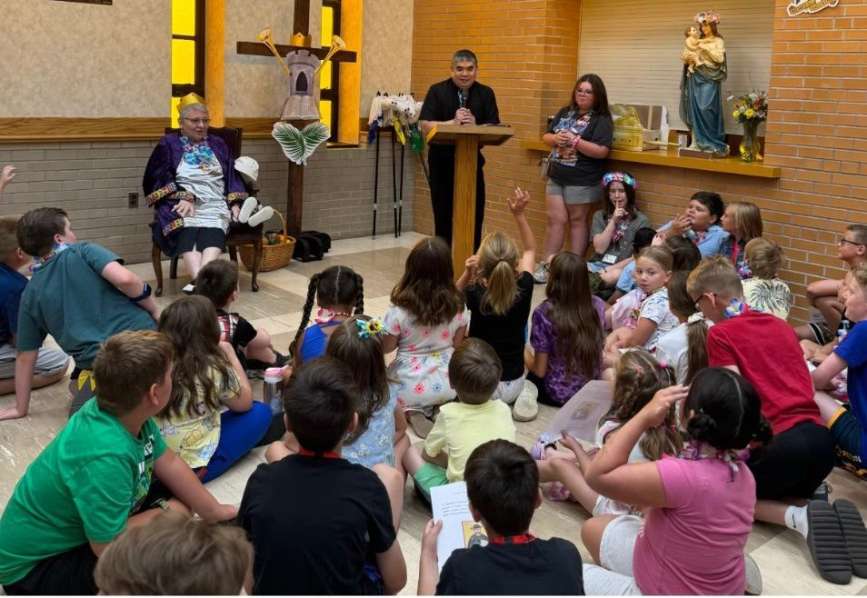A priest speaks to a group of children gathered inside a church.
