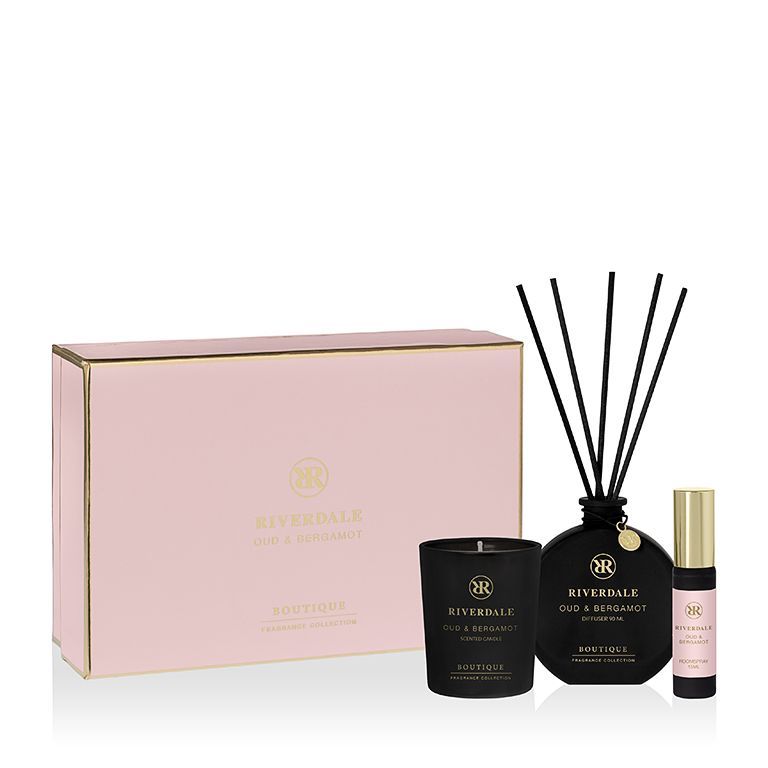 Roze geschenkdoos met zwarte geurstokjes, kaars en klein parfumflesje op een witte achtergrond.