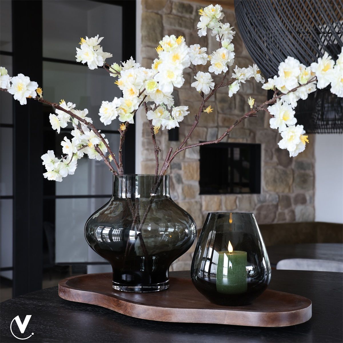 Witte bloesem in donkere glazen vazen op een houten dienblad in een moderne woonkamer.