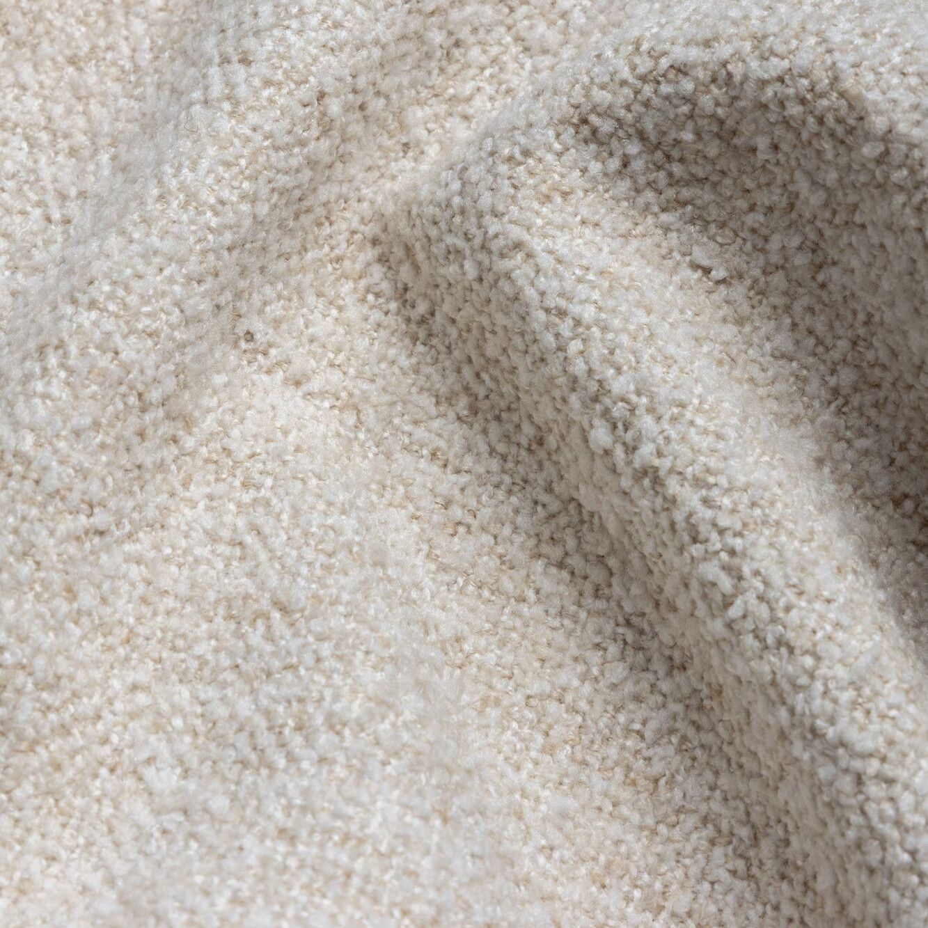 Detailopname van een beige, gestructureerde stof met zachte plooien en schaduwen.
