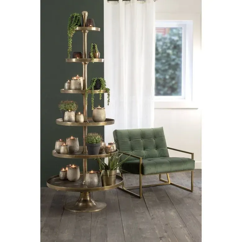 Een hoge, etagère met kaarsen, planten en een groene fluwelen stoel in een kamer met een raam.