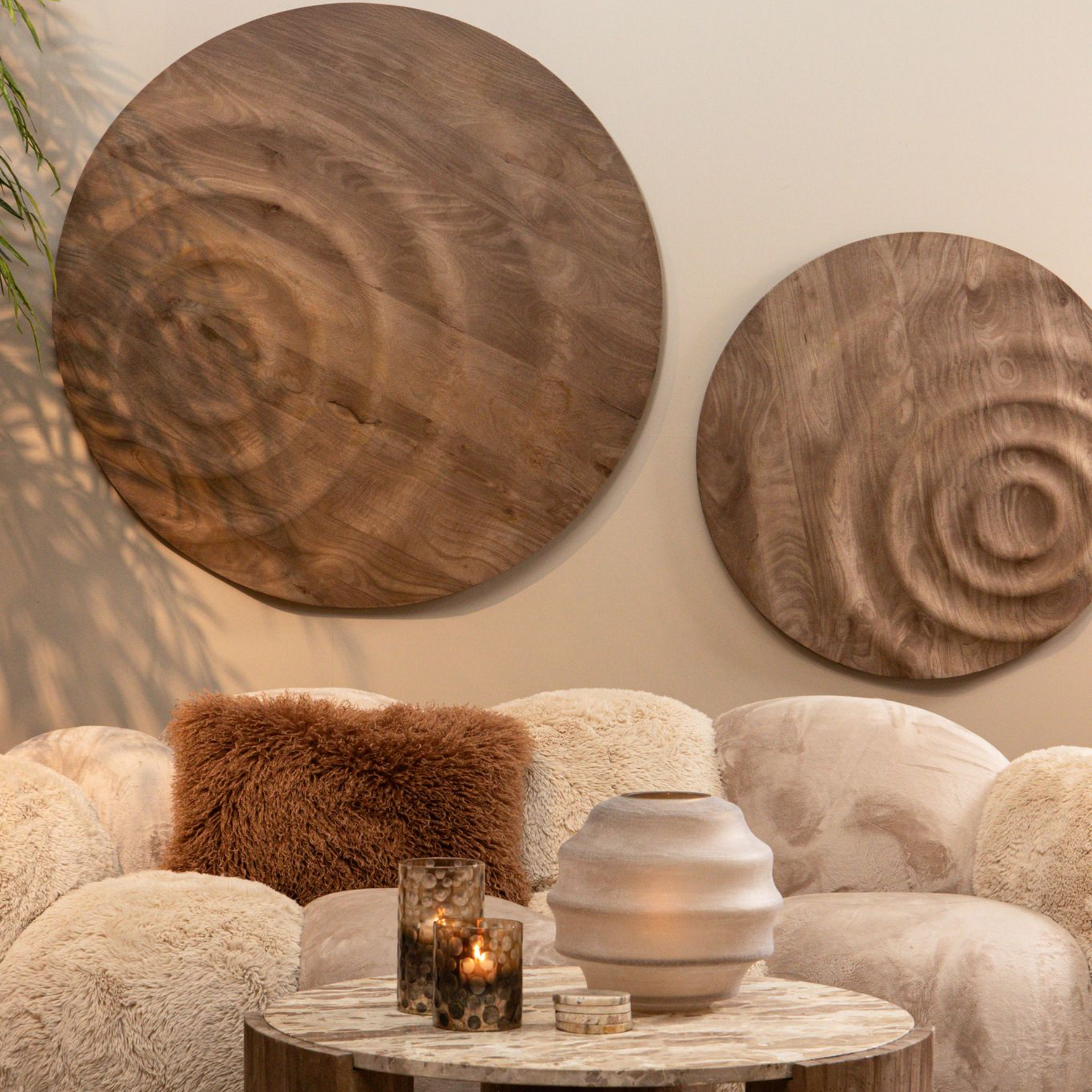 Twee ronde houten wanddecoraties boven een bank met structuur en een salontafel.